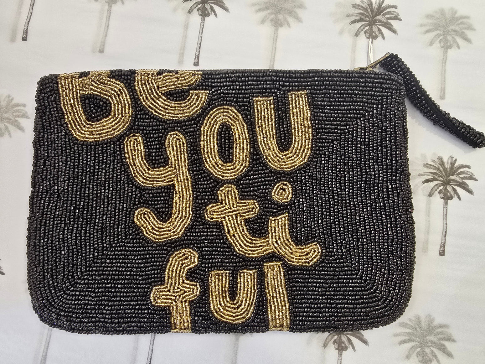 Black beaded clutch with gold text 'Be You Ti Ful' on a patterned background